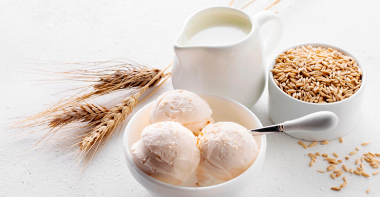 Sorvete vegano: bowl com duas bolas de sorvete que parece vegano. Do lado do bowl, há um recipiente com leite e outro com grãos que parecem trigo.