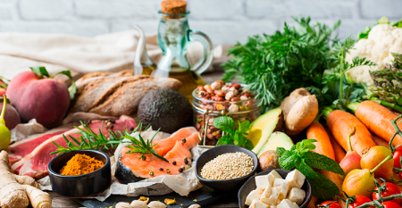 Alimentos diet: vários alimentos dispostos sobre uma mesa de madeira. Há ingredientes como salmão, cenoura, tomates, gengibre, pistache, entre outros.  